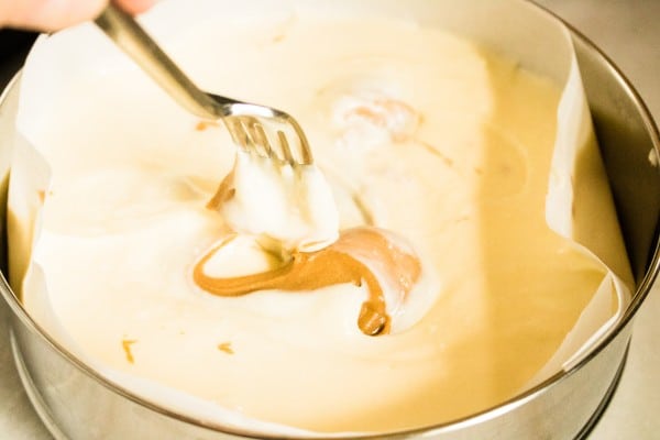 a fork being used to swirl peanut butter into cheesecake mixture in a springform pan