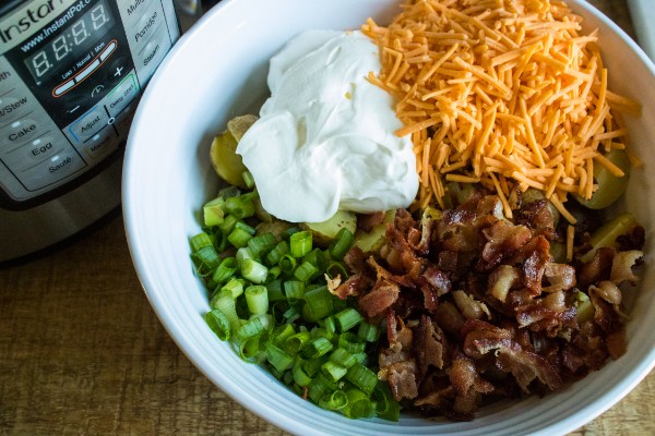 potatoes: bacon, cheese, sour cream, green onions, and mayonnaise in a white bowl on a brown table next to an instant pot