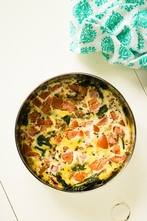 blt frittata in a round metal pan on a white wood table with a green and white cloth in the background