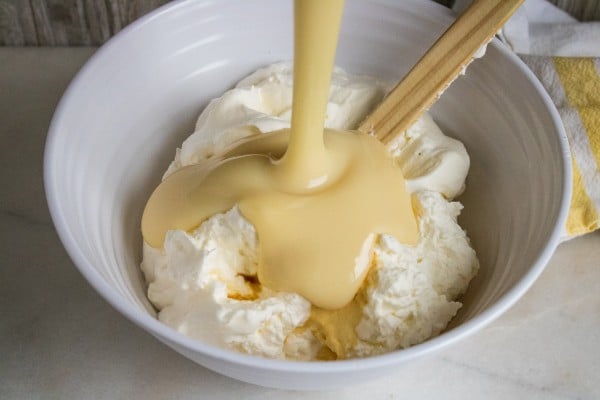 condensed milk being poured into a white bowl of fluffy whipped cream