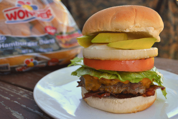 USO burger on a white plate on a brown table with a bag of wonder hamburger buns and camouflage clothing in the background