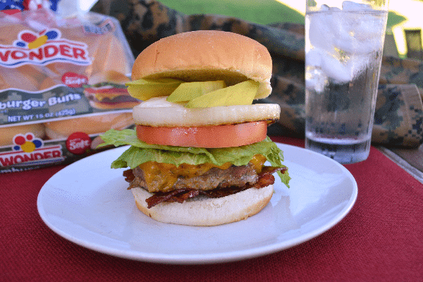 USO burger on a white plate on a red cloth with a bag of wonder hamburger buns, a glass of water and camouflage clothing in the background