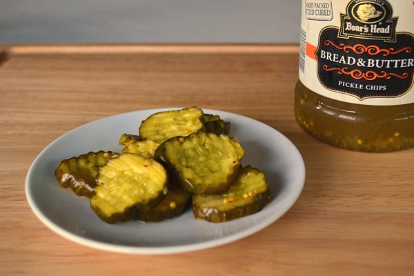 a plate with bread and butter pickle chips on it next to the jar of pickles on a wood table
