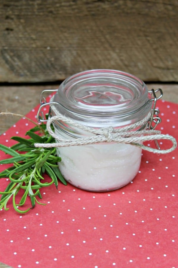 DIY makeup wipes in a glass jar with a white string tied on it in a bow next to a green sprig on a red and white polka dotted cloth on a brown table