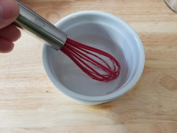 using a whisk to blend the ingredients for a diy makeup remover in a white bowl on a brown table
