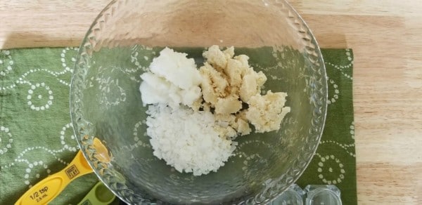 shea butter, coconut oil and beeswax in a glass bowl on a green linen on a wood table
