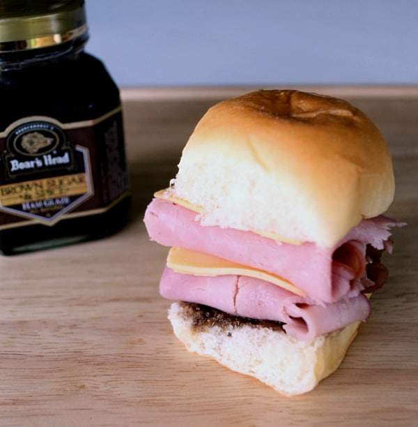 a ham and cheese slider next to a jar of Boar's Head Brown Sugar & Spice Ham Glaze on a brown table
