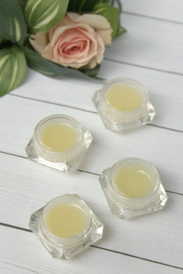 four jars of homemade eye cream on a white wood table with a flower in the background 