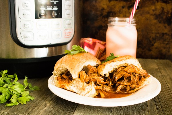 bbq shredded chicken sandwich on a plate with a mason jar drink and instant pot in the background