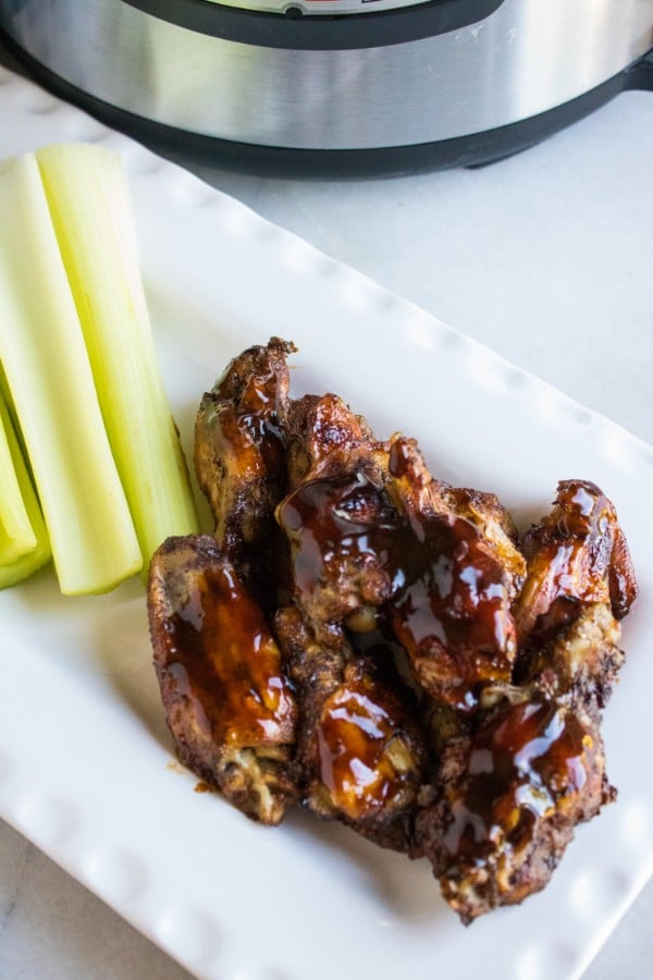 chicken wings covered in sauce next to celery sticks on a white tray on a white table with an instant pot in the background