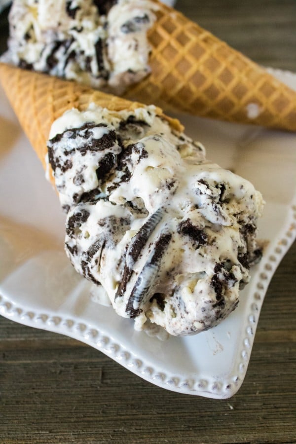 a close up of two waffle cones full of oreo ice cream on a white plate on a brown table with a gray linen on the background 
