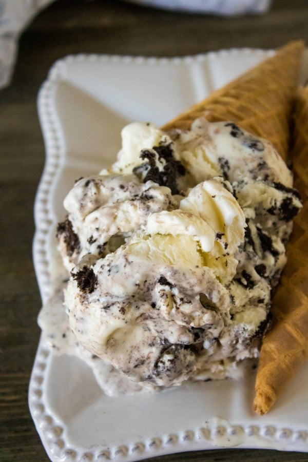 a closeup of two waffle cones full of oreo ice cream on a white plate on a brown table with a gray linen on the background 