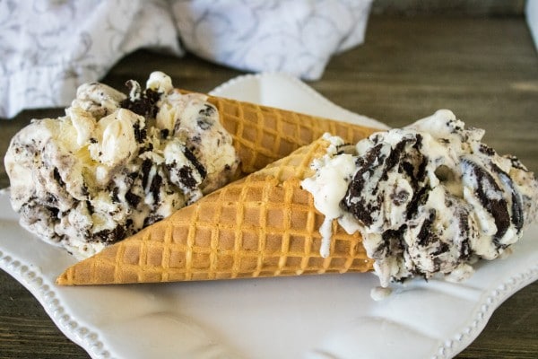 two waffle cones filled with oreo ice cream on a white plate on a wood table with a white and gray cloth in the background