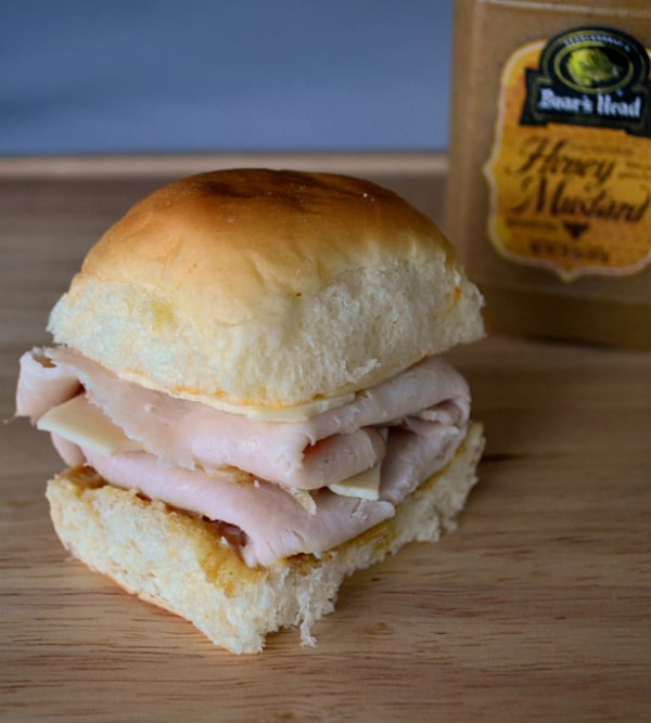 a turkey and cheese slider next to a jar of Boar's Head Honey Mustard on a brown table