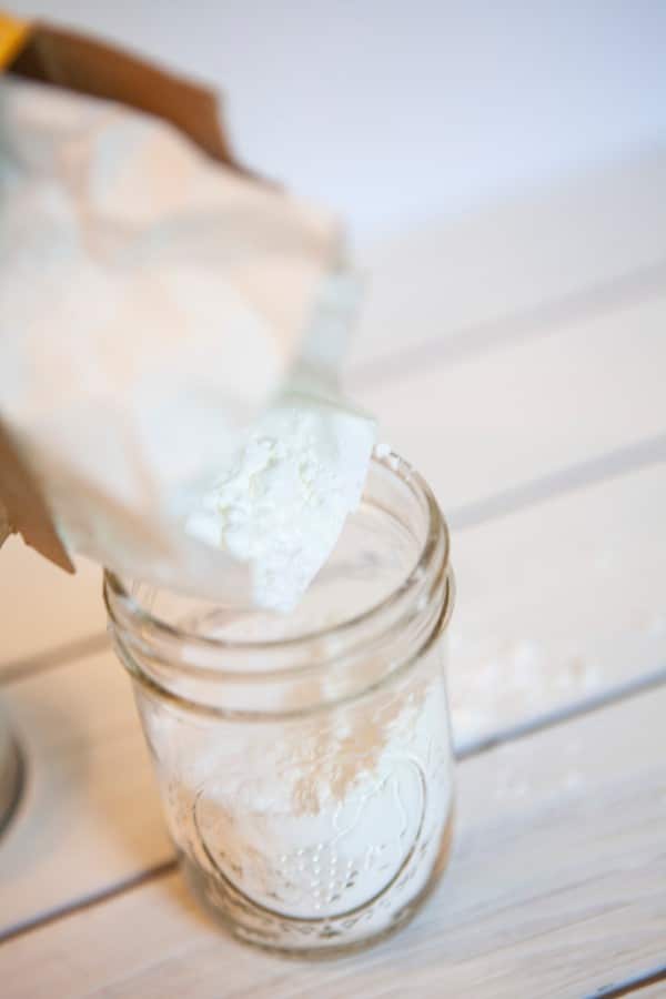 pouring cornstarch into a glass mason jar on a white wood table