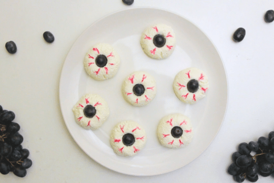cottage cheese and olives decorated to look like eyeballs on a white plate on a white table with more olives around the plate