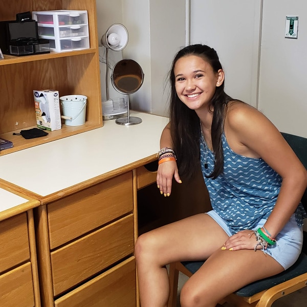 a girl sitting at a desk in a college dorm room