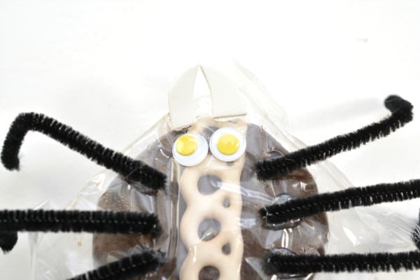 a packaged cupcake decorated with black pipe cleaners as legs, to look like a spider on a white background 