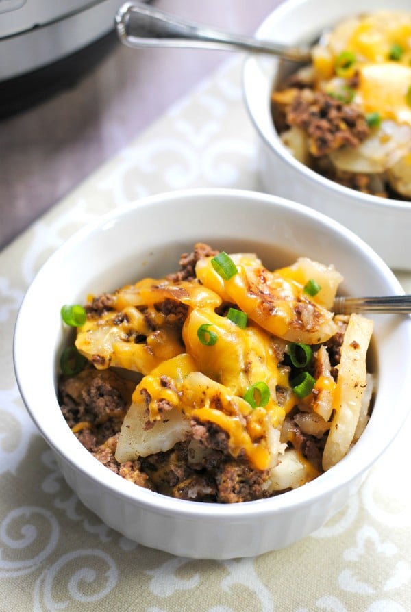cheesy hamburger potato casserole in a white bowl with a spoon in it on a brown cloth with another bowl and an instant pot in the background 