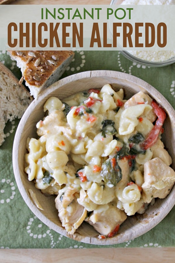 chicken alfredo in a brown bowl on a green linen next to a buttered piece of bread and a small glass bowl of parmesan cheese, all on a brown table, with title text reading Instant Pot Chicken Alfredo
