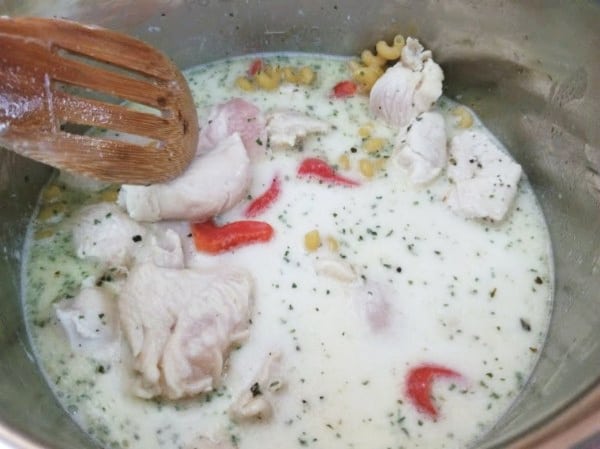 cubed chicken, Alfredo sauce, chicken broth, roasted red peppers, and pasta being stirred with a wooden spoon in an instant pot
