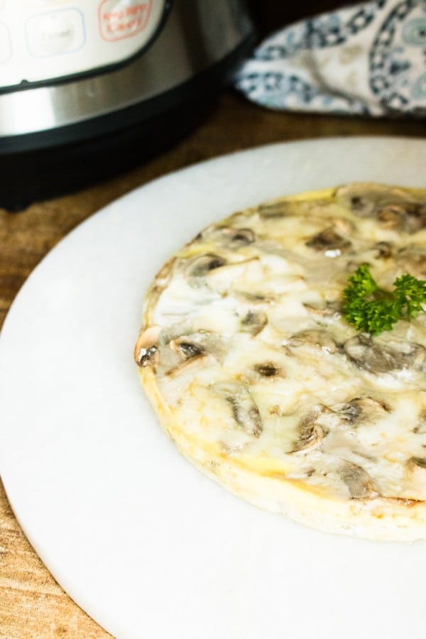 mushroom and swiss frittata on a white plate on a wood table next to an instant pot in the background 