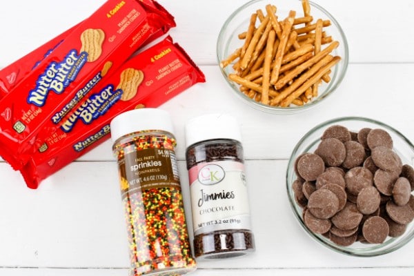 packages of nutter butter cookies, jars of sprinkles, glass bowls of pretzel sticks and chocolate candy melts on a white wood table