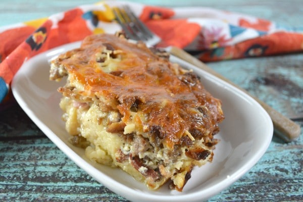 a breakfast casserole in a white dish on a wood table with a fork and flower cloth in the background 