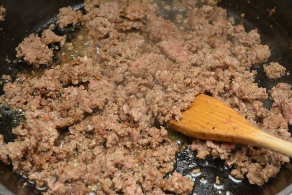 sausage cooking in a skillet with a wooden spoon