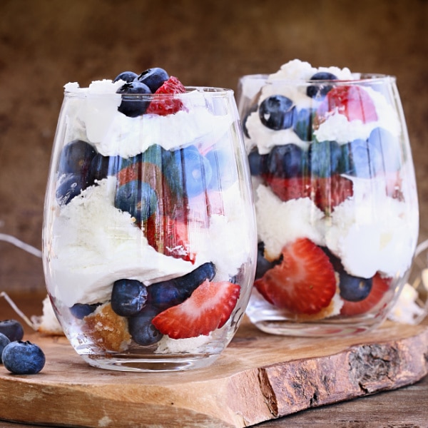 two glasses filled with strawberries, blueberries, and yogurt on a piece of wood