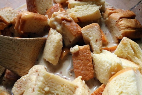 cubed bread in a bowl of the wet ingredients for bread pudding