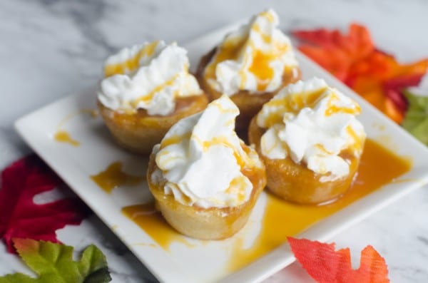 caramel pumpkin cookie cups topped with whipped cream on a white plate on a counter with some leaves around it