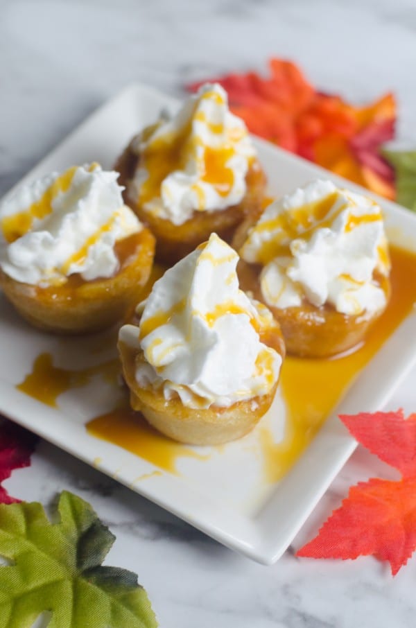 baked cookie cups filled with canned pumpkin, topped with whipped cream and caramel sauce on a white plate on a white counter with fake leaves around the plate 