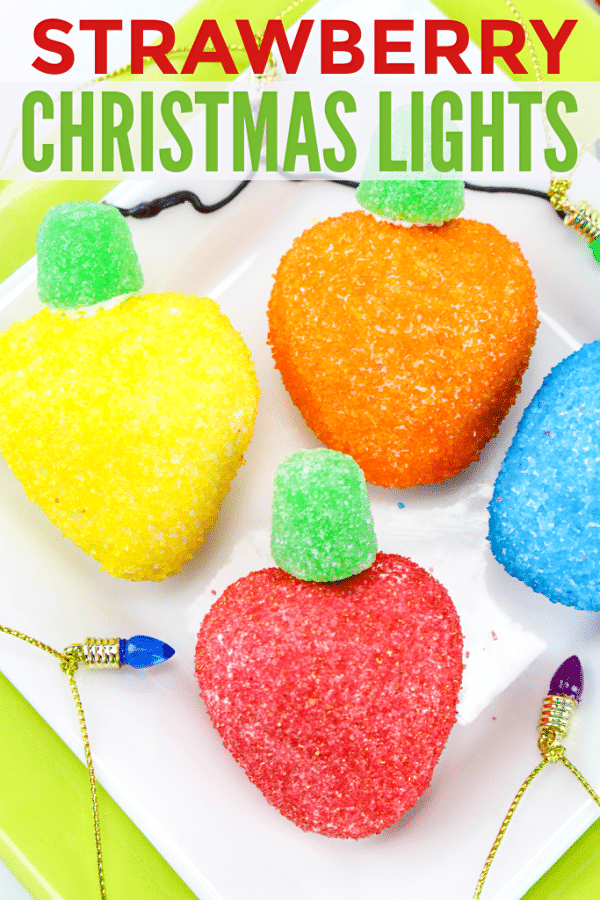 strawberries coated with colored sugar with a green gumdrop on top to look like Christmas lights on a white and yellow plate surrounded by mini Christmas lights on a gold chain with title text reading Strawberry Christmas Lights