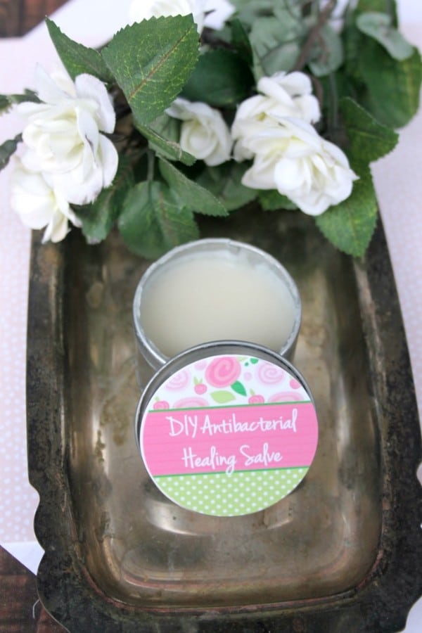 DIY Healing Salve in a container next to some white flowers on a metal tray