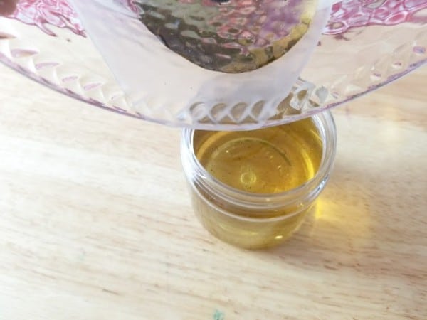 pouring the salve from the glass bowl into a smaller glass container on a wood table
