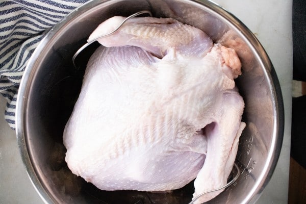 a turkey with the wings held down by a metal trivet in an instant pot