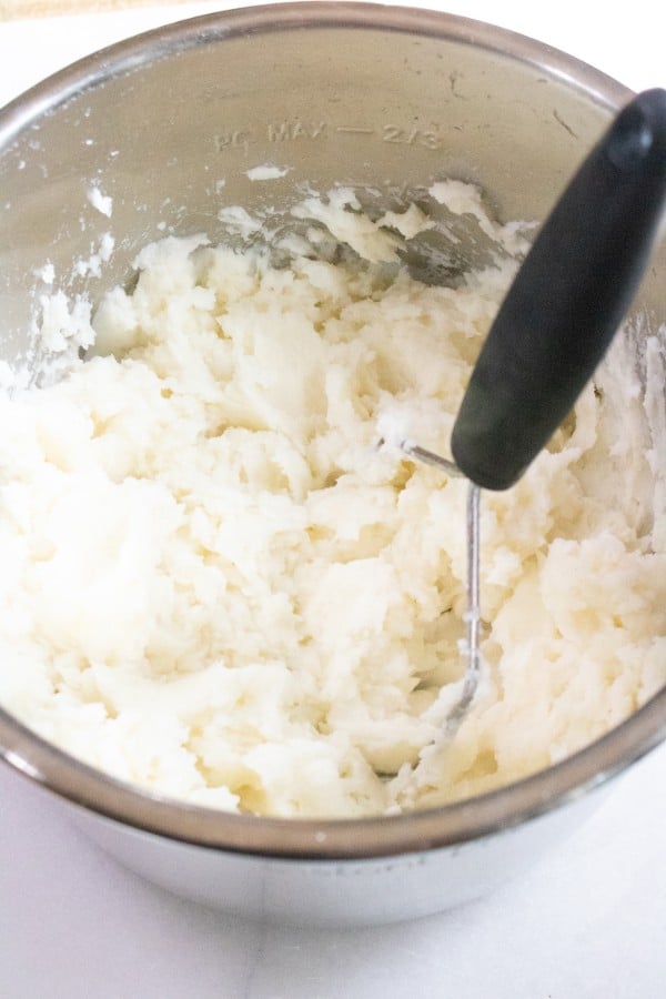 potatoes being mashed with a potato masher in an instant pot on a white counter