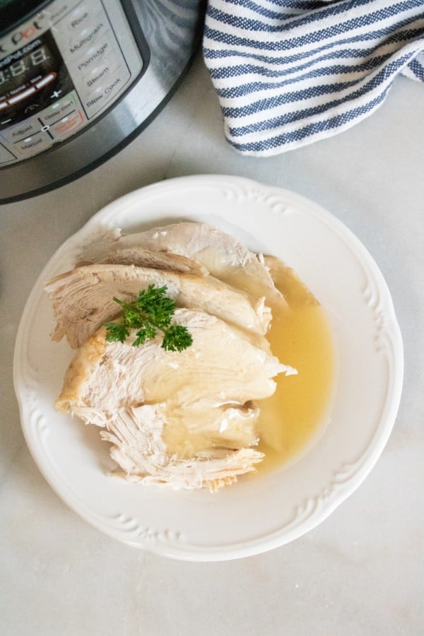overhead view of pieces of turkey topped with gravy and parsley on a white plate on a white table with an instant pot and striped linen in the background 