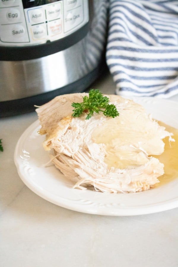 a piece of turkey topped with gravy and parsley on a white plate on a white table with an instant pot and striped linen in the background 