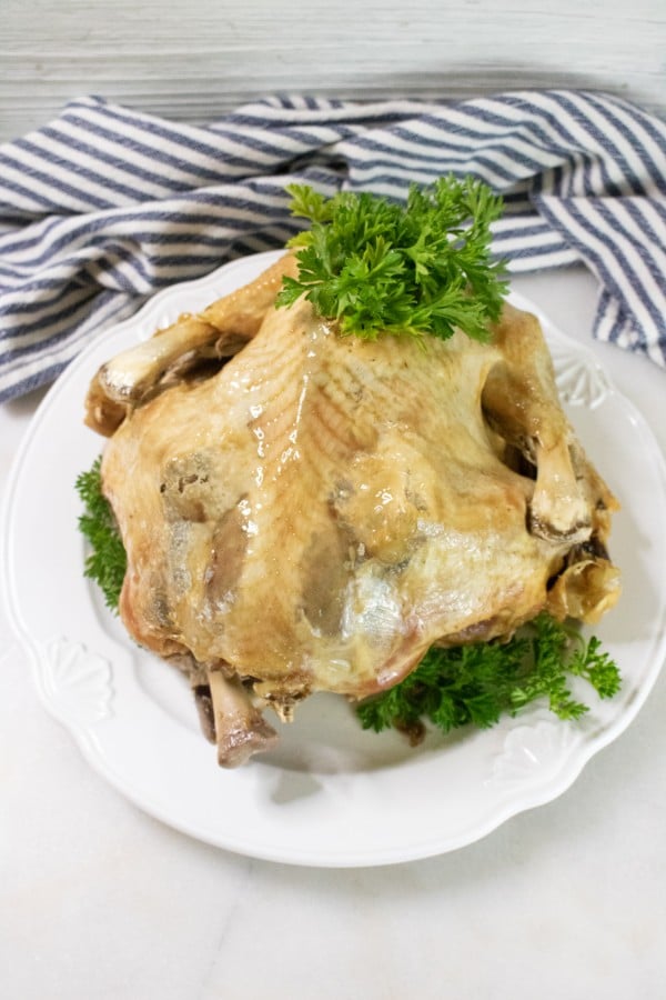 a whole turkey topped with parsley on a white plate on a white table with a striped linen in the background 