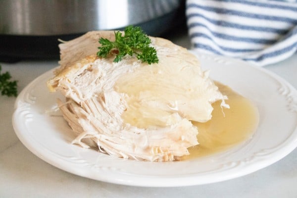 turkey topped with parsley and gravy on a white plate on a white counter with an instant pot and blue and white linen in the background