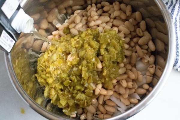 chicken stock being poured into an instant pot inner liner filled with cooked turkey, diced onions, beans and green chilis