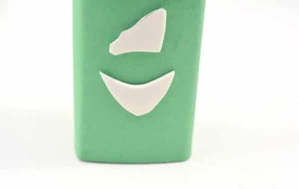 a juice box wrapped with green construction paper with white foam glued on to look like a nose and mouth on a white background