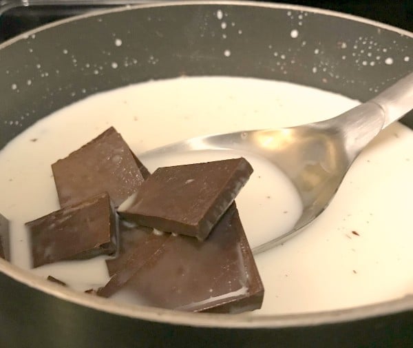 milk and chocolate in a saucepan being stirred with a spoon
