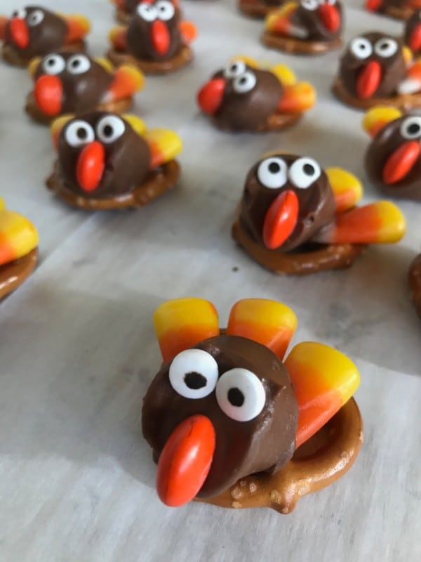pretzels on a wood table topped with rolos decorated with candy eyes, an M&M nose, candy corn feathers to look like a turkey 