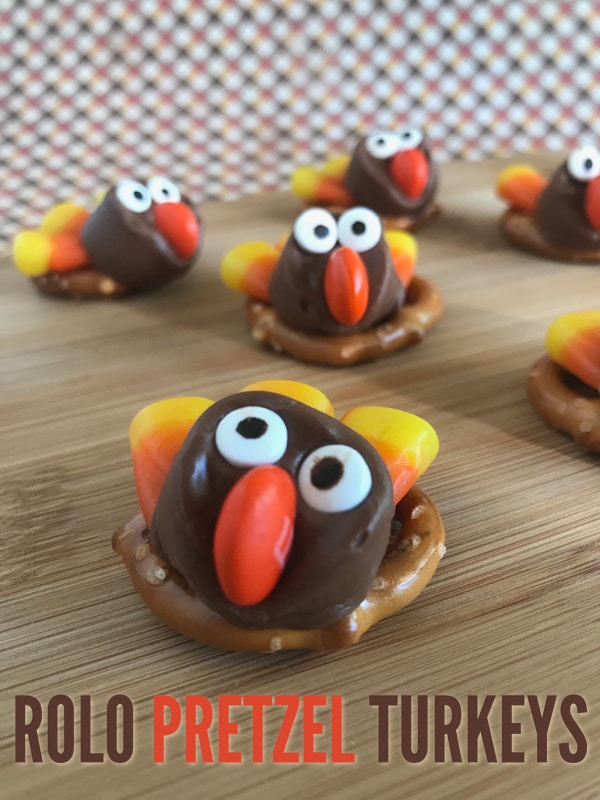 pretzels on a wood table topped with rolos decorated with candy eyes, an M&M nose, candy corn feathers to look like a turkey with title text reading Rolo Pretzel Turkeys