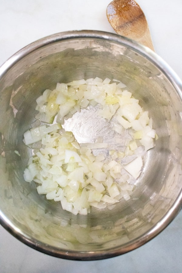 overhead view of garlic and onions in an instant pot next to a wooden spoon on a white counter