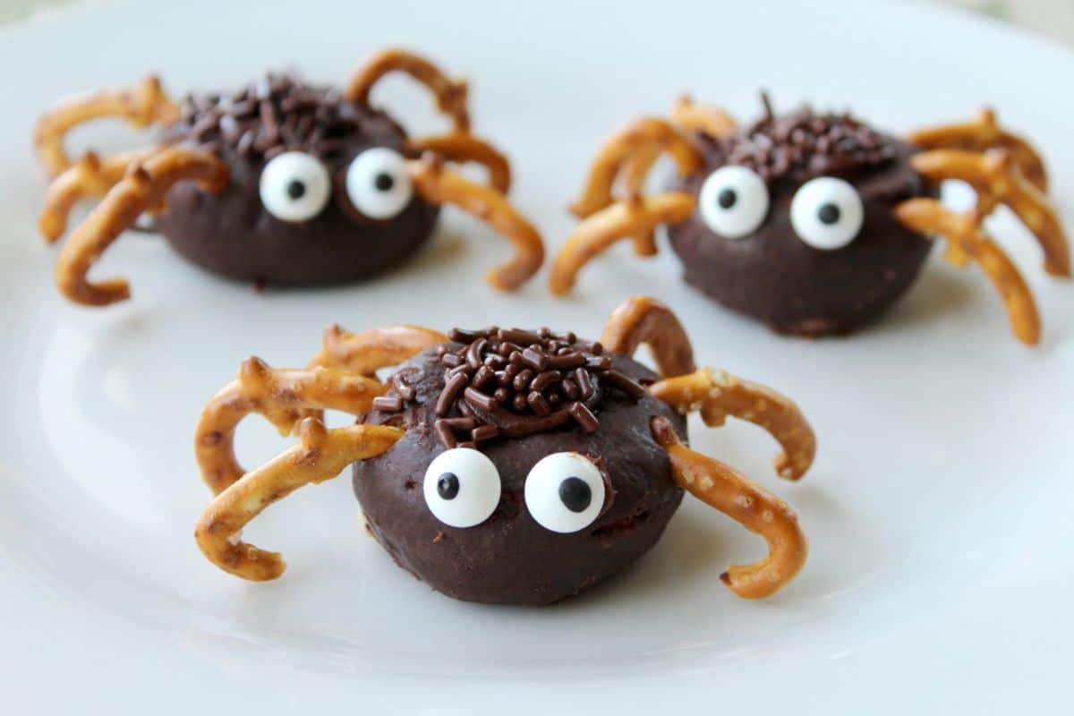 Three mini donut spiders on a plate with pretzels.