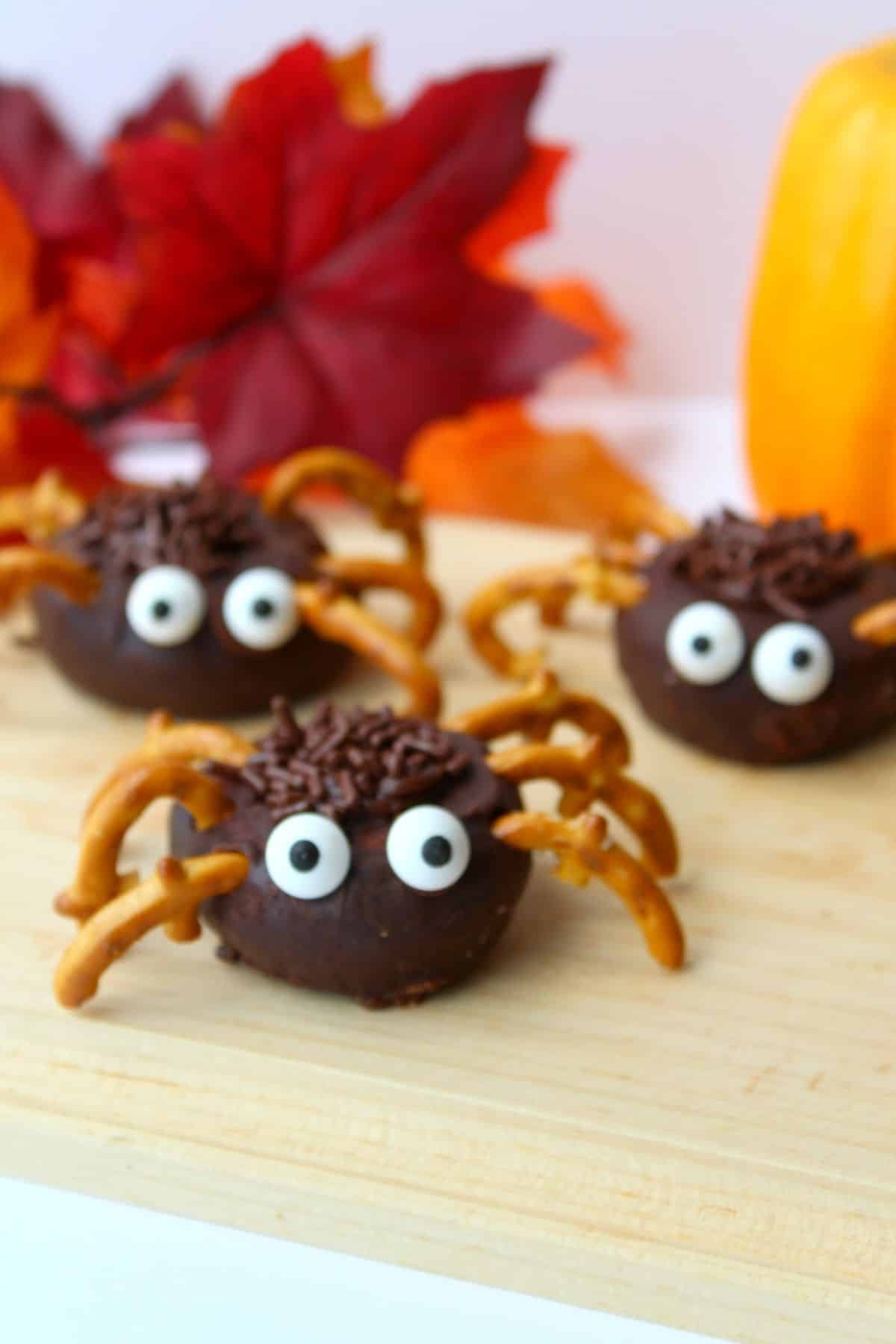 Mini chocolate spiders on a wooden cutting board.